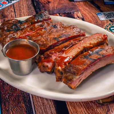 Rack of ribs served on a white plate with a side of sauce.