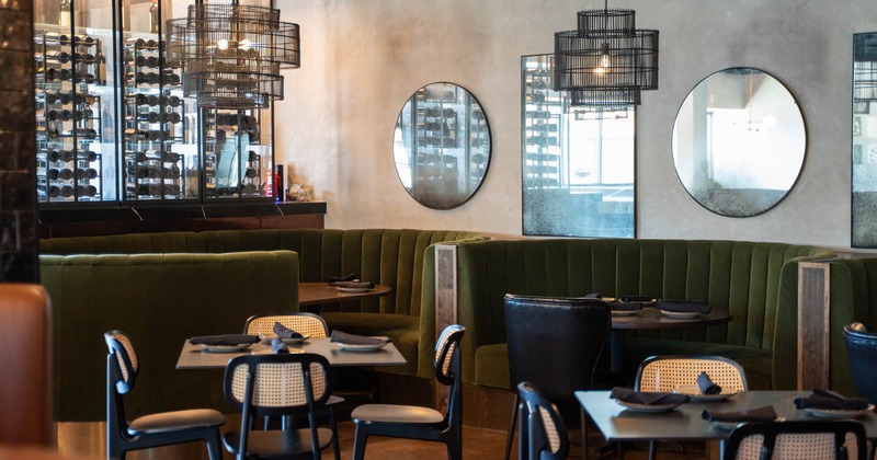 Interior of a modern restaurant with green velvet banquettes, black chairs, and wine display