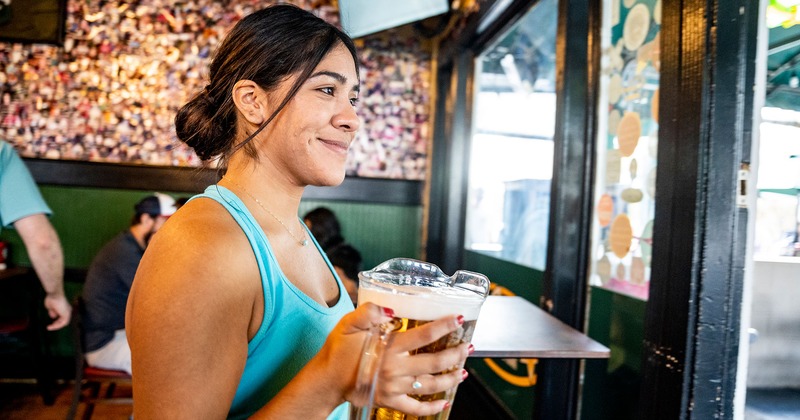 A waitperson holds a large beer pitcher, smiling in a lively restaurant setting