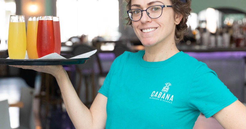 A smiling server posing for a shot while holding a tray with Mimosas