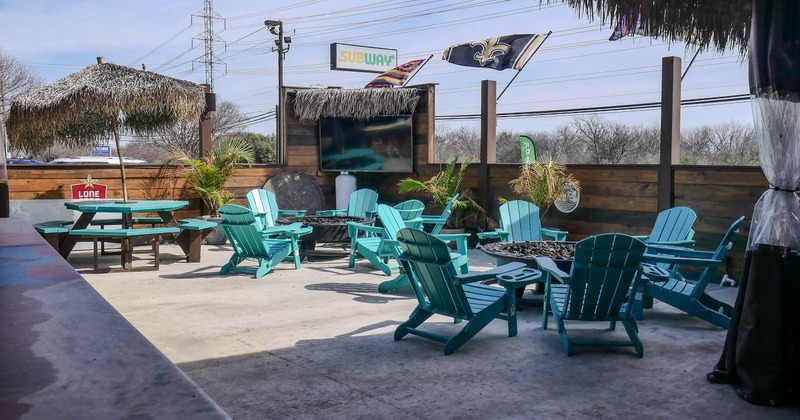 Exterior, seating area, blue wooden chairs around fire pits, hay parasols, large TV