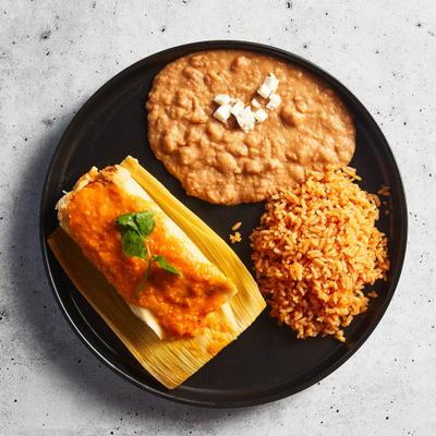 A plate featuring a tamales, accompanied with refried beans and rice.