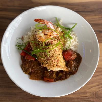 A dish of fish and shrimp served over rice with a rich, dark sauce