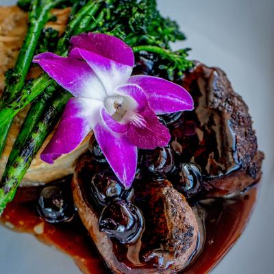 Seared meat, blueberries, broccolini, a purple orchid and pastry, close up.