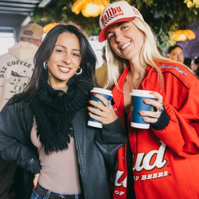 Two persons posing for a photo with take away coffee cups.