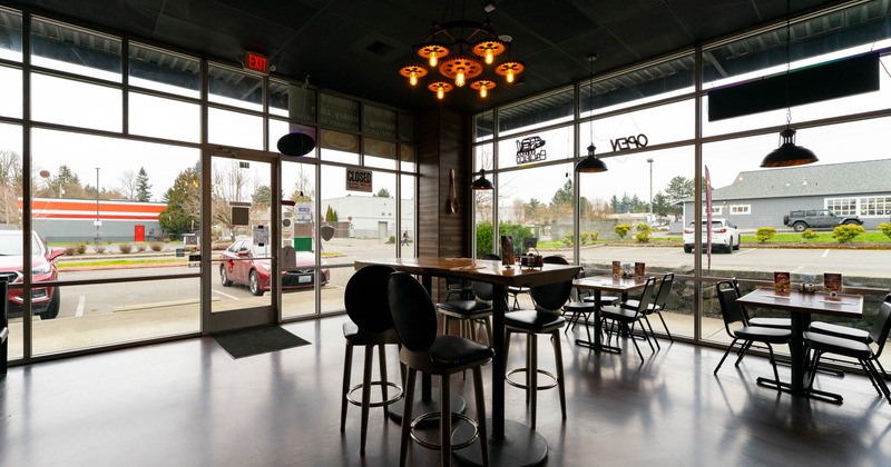 Interior with tables, chairs, a unique chandelier, and large windows facing a parking lot