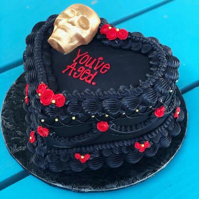 Black heart shaped cake with miniature red decorations and a skull figurine on top