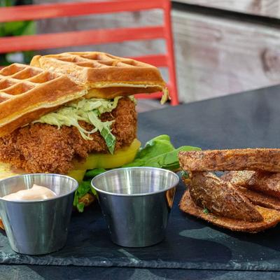 Chicken waffle sandwich served  with maple syrup, spicy sauces, and potato wedges.