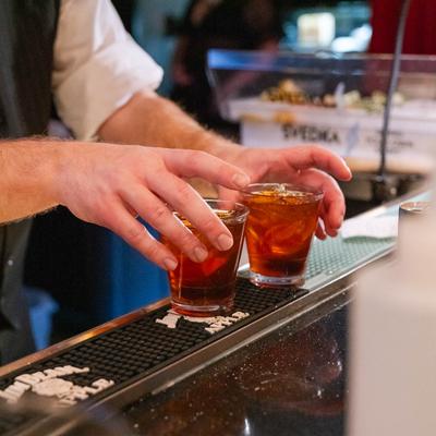 A bartender places drinks on bar counter mat.