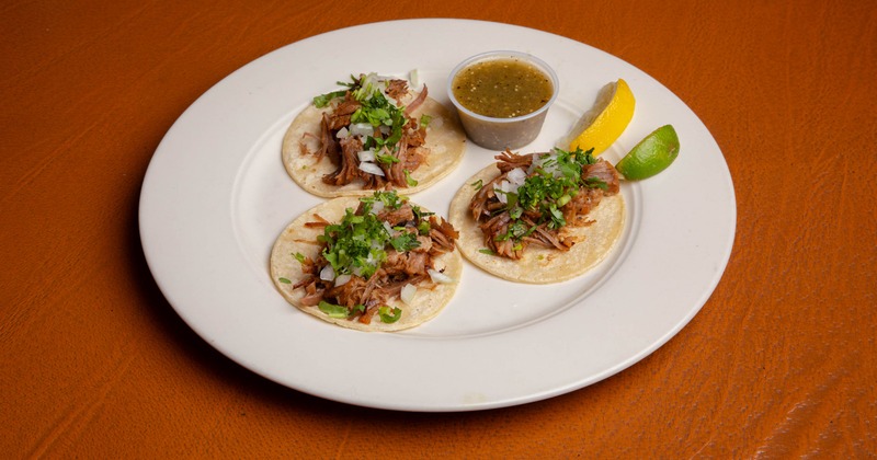 Street tacos served with a cup of salsa verde and citrus wedges