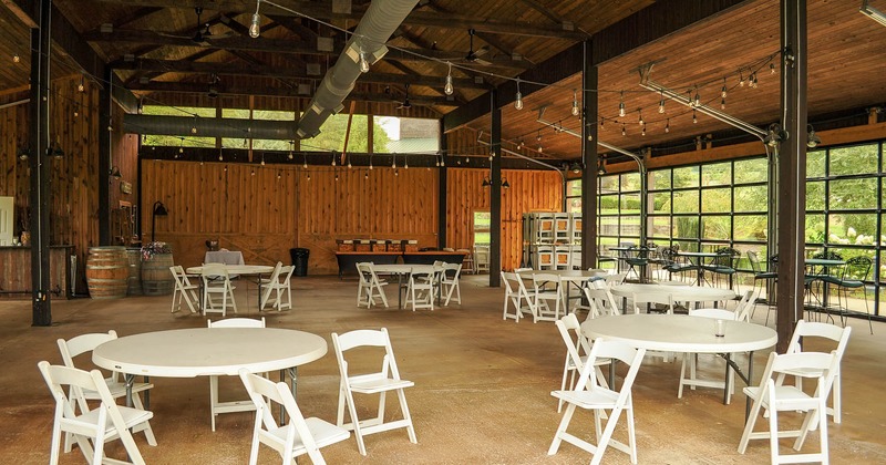 Interior, rustic barn like space with white round tables and folding chairs