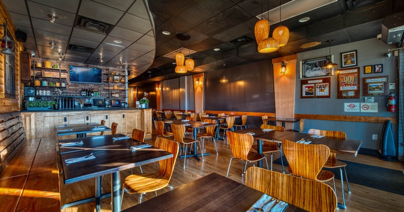 Interior of a modern restaurant with wooden tables and chairs, a bar, pendant lights