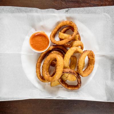 Onion rings served with a cup of red dipping sauce.