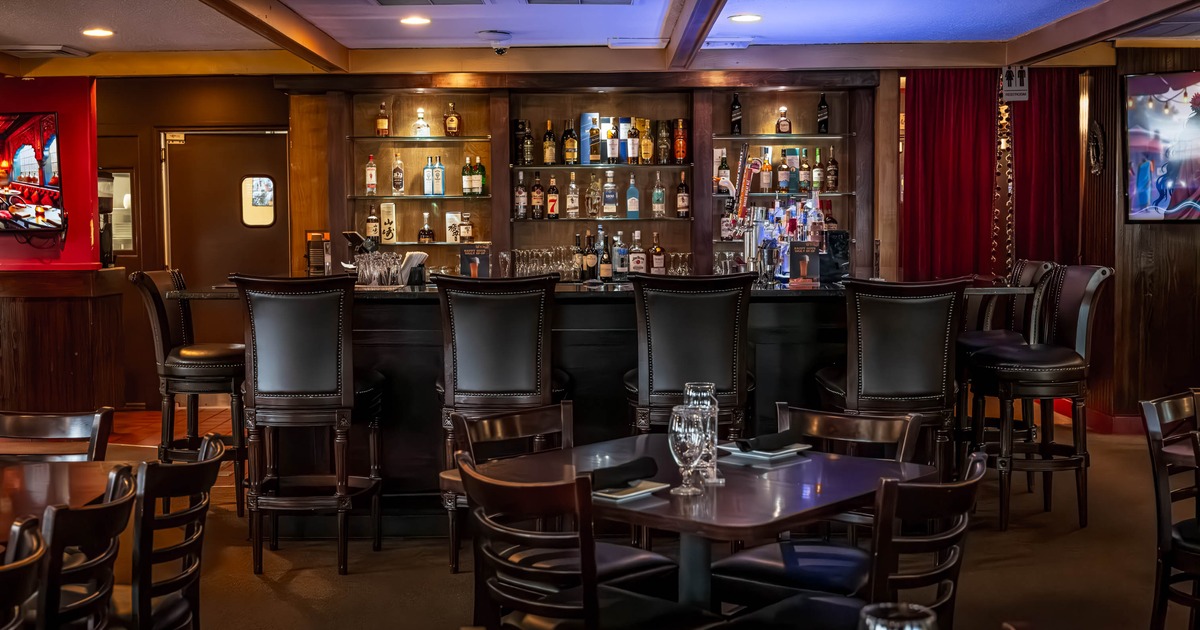 A cozy bar interior with a wooden counter, bar stools, stocked liquor shelves and warm lighting