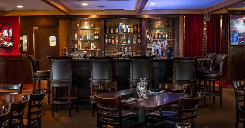 A cozy bar interior with a wooden counter, bar stools, stocked liquor shelves and warm lighting