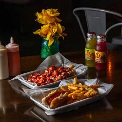 Kids Hot dog with fries and a plate with pan fried sausages on a table.