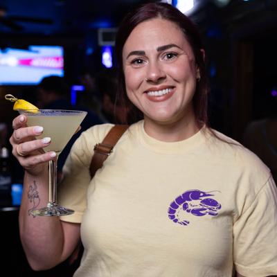 A smiling customer holds a martini glass filled with a cocktail drink.