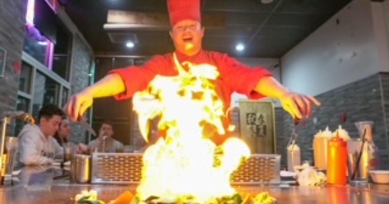 A chef performing a fire trick on a flat iron griddle