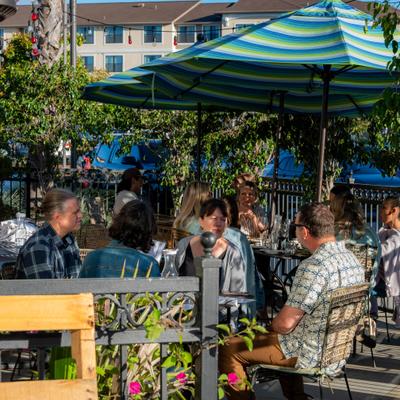 Outdoor patio dining area with patrons seated at tables under striped umbrellas.