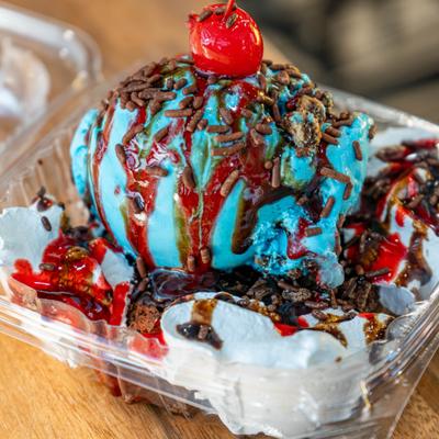 Brownie split topped with vibrant blue ice cream, chocolate sprinkles, and maraschino cherry.
