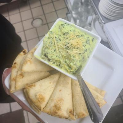 A hand holding a plate with spinach dip and pita bread.