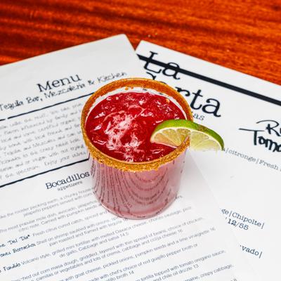 Cocktail in chili-rimmed glass with a slice of lime, served over menues.