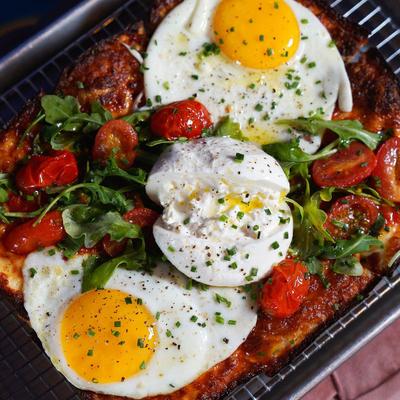 Pizza with cheeses, fried eggs, burrata, arugula, and roasted tomatoes.