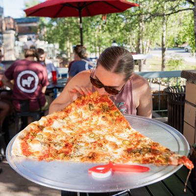 A person enjoys a giant slice of pizza outdoors.