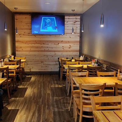 Interior, seating area with wooden tables and chairs, and a TV screen on a wooden wall.