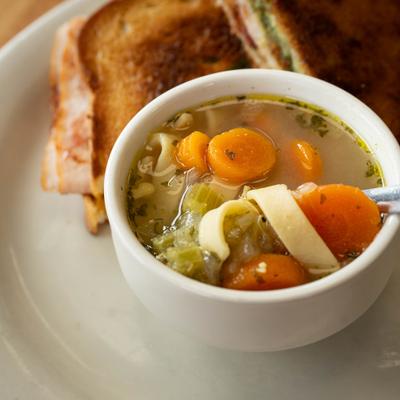 Bowl of chicken noodle soup with carrots and celery alongside a toasted sandwich.