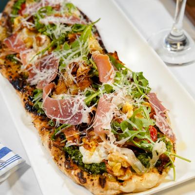Prosciutto and arugula flatbread with Parmesan and pesto sauce.