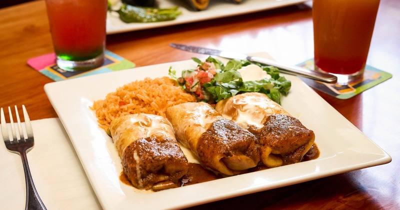 Three burritos alongside rice and fresh salad