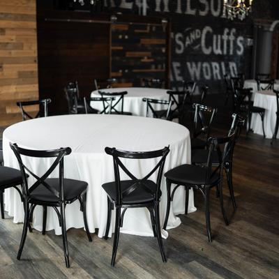 Round banquet tables with white tablecloths and black crossback chairs.