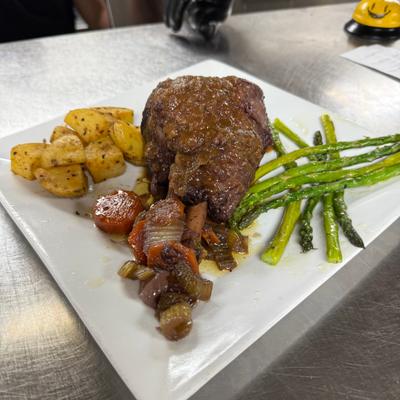 Beef steak accompanied by asparagus spears, roasted potato, and sautéed mushrooms and tomatoes.