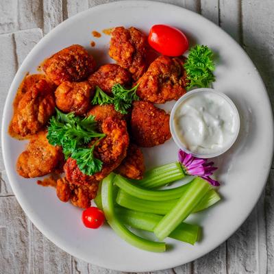 Crispy boneless chicken wings with celery sticks, ranch dipping sauce, and parsley garnish.