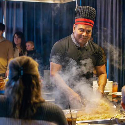 A friendly chef cooking food for the customers at a table.
