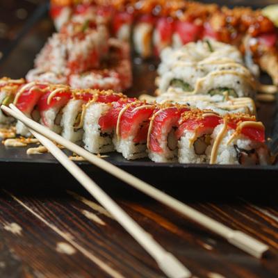 Sushi rolls on black plate with chopsticks.