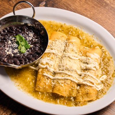 Green enchiladas drizzled with crema served with black beans topped with fresh cheese.