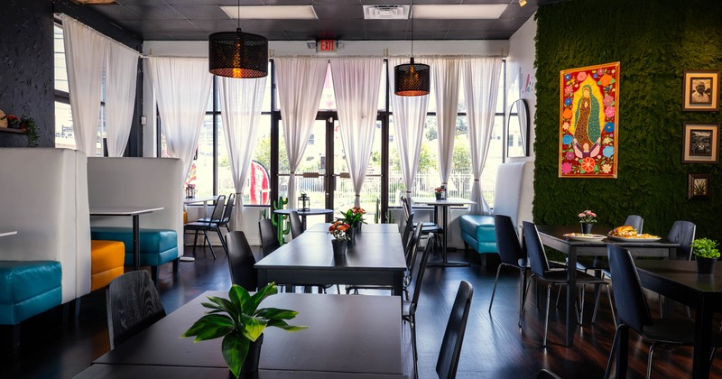 Interior with large windows, colorfully decorated walls, and various seating arrangements, including teal and orange booths