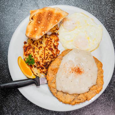 Country fried steak served with fried eggs, hash browns, toast, and gravy.
