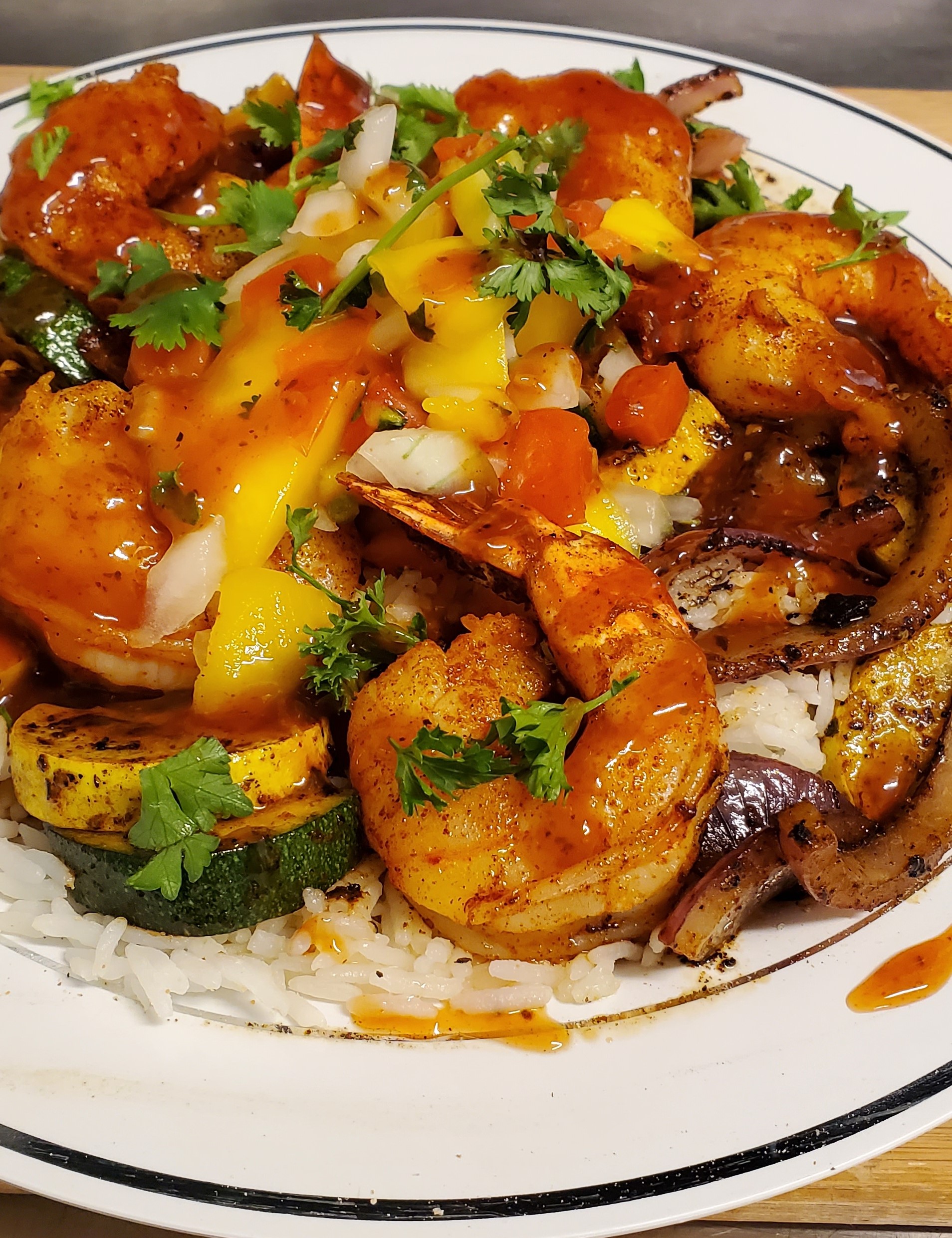 Plate with rice, vegetables, large grilled shrimp and mango salsa.