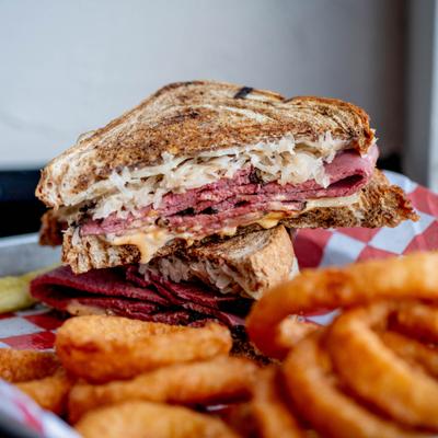 Reuben sandwich sliced in half served with a side of onion rings.