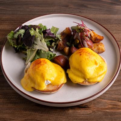 Eggs Benedict served with potatoes and mixed greens.