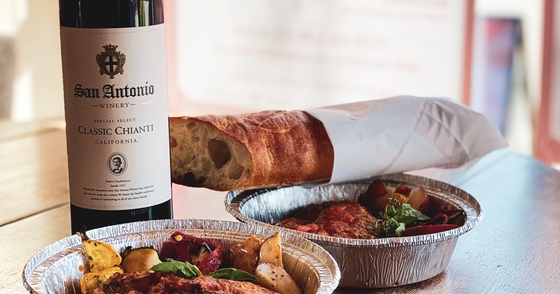 Two dishes in takeaway containers with bottle of wine