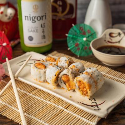 Spicy Tuna Roll accompanied by chopsticks, a bowl of soy sauce, and a bottle of sake.