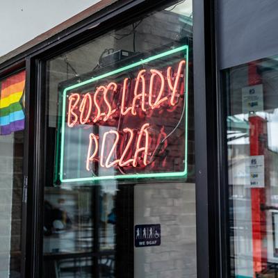 Close-up of a storefront with neon business name and a rainbow flag.
