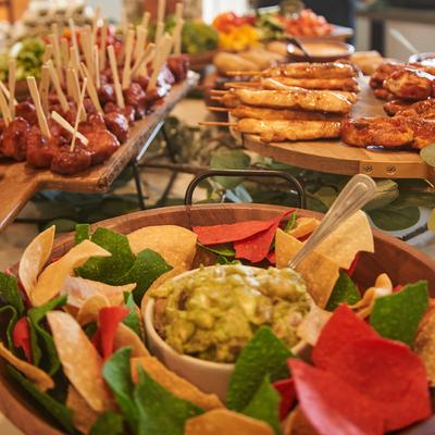 A large bowl of tortilla chips with a central bowl of guacamole, and meat skewers.