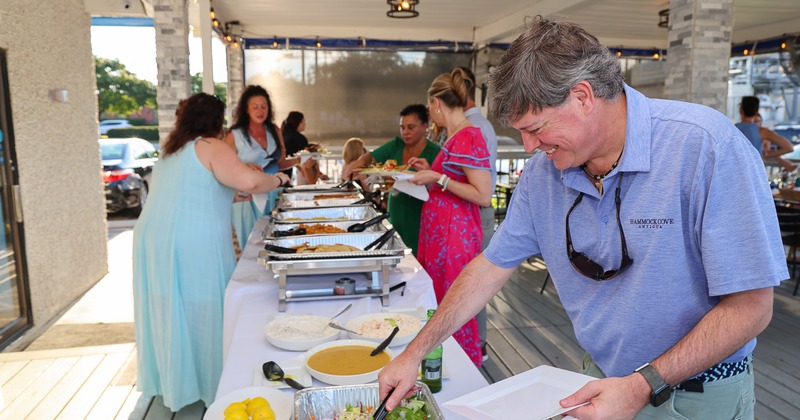 People serving themselves from a buffet on a covered patio during a daytime event