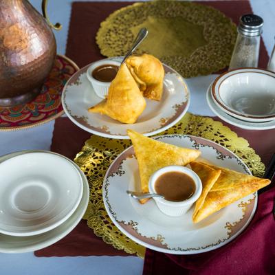 Golden-brown samosas served with a dipping sauce, on ornate white plates.