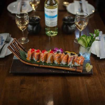 Sushi roll served on decorative board with garnish and white wine.